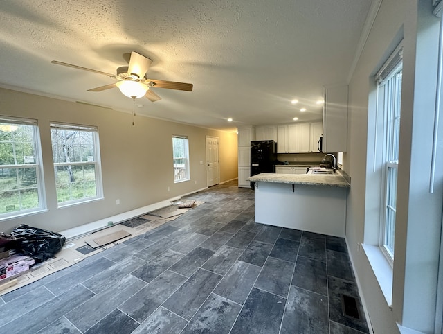 kitchen with ceiling fan, white cabinets, black fridge, sink, and kitchen peninsula