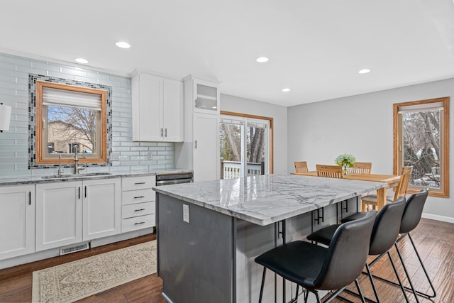 kitchen with a kitchen island, a sink, a kitchen breakfast bar, light stone countertops, and dark wood-style floors