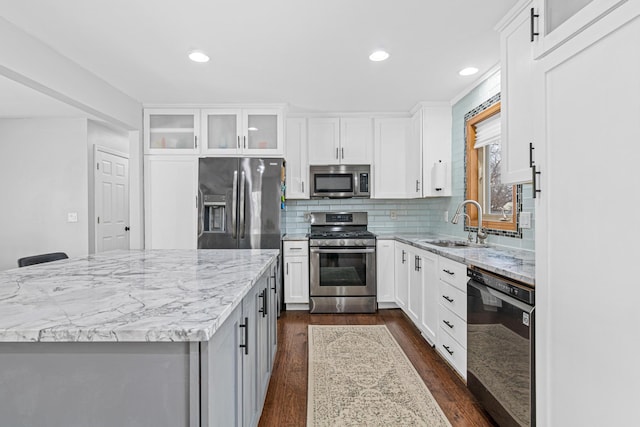 kitchen with tasteful backsplash, dark wood-style floors, appliances with stainless steel finishes, light stone counters, and a sink