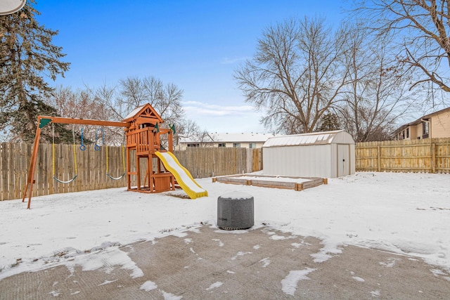 snow covered playground with a fenced backyard, an outbuilding, a playground, and a shed