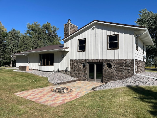 rear view of property featuring central AC unit, a lawn, a patio area, and an outdoor fire pit