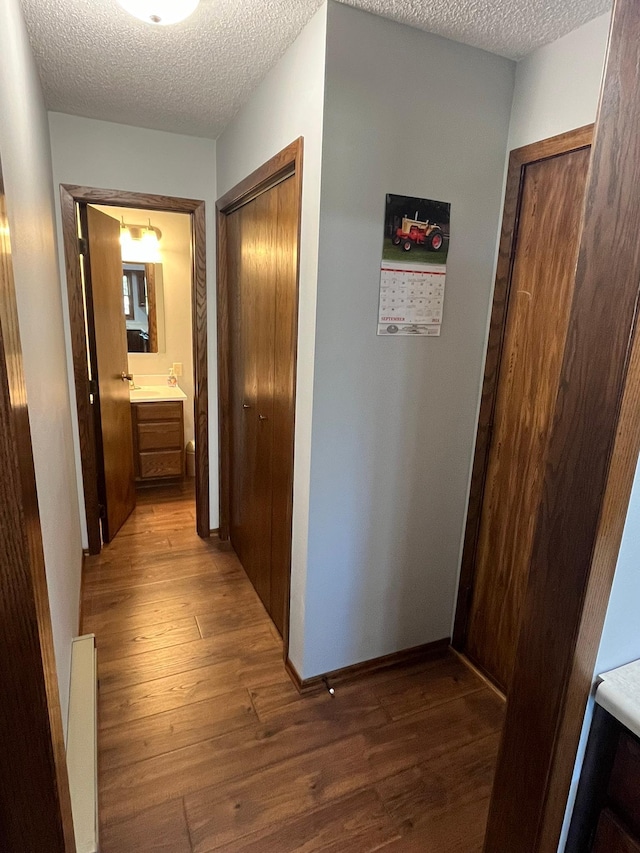 hallway featuring a textured ceiling, baseboard heating, and dark hardwood / wood-style flooring