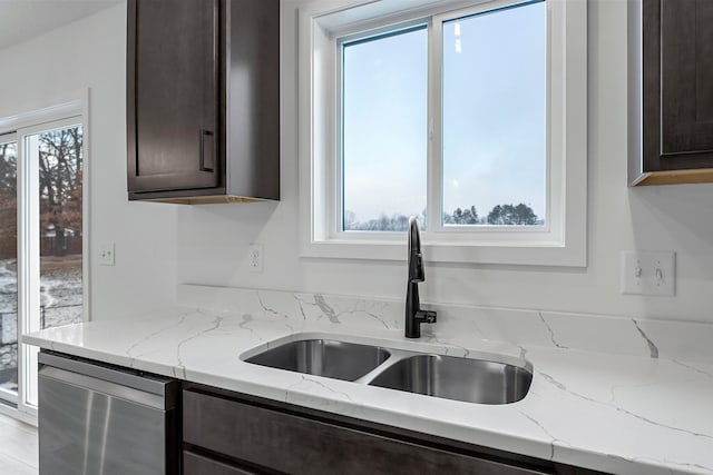 kitchen with light stone countertops, dark brown cabinets, stainless steel dishwasher, and sink