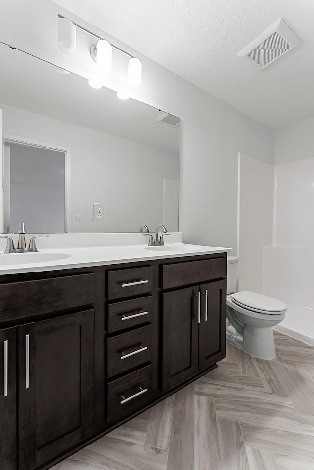 bathroom featuring walk in shower, vanity, a textured ceiling, and toilet