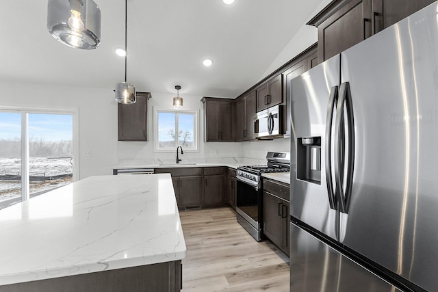 kitchen featuring sink, stainless steel appliances, light stone counters, light hardwood / wood-style flooring, and decorative light fixtures