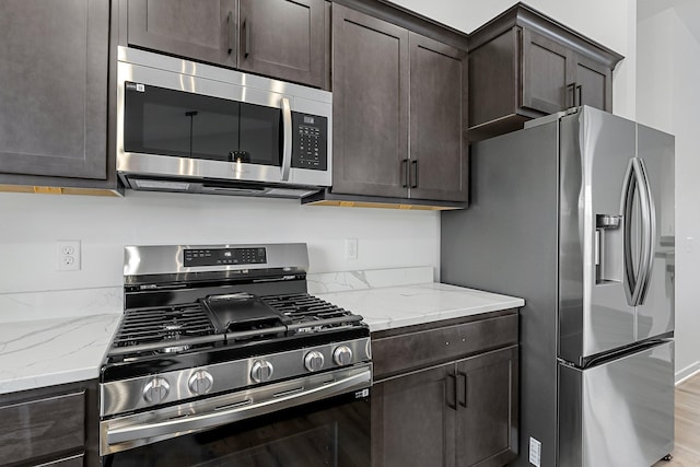 kitchen with dark brown cabinets, light stone countertops, appliances with stainless steel finishes, and light hardwood / wood-style flooring