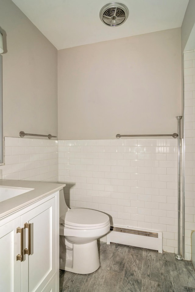 bathroom with tile walls, a baseboard heating unit, hardwood / wood-style flooring, vanity, and toilet