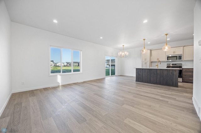 unfurnished living room featuring a chandelier, light wood-type flooring, baseboards, recessed lighting, and a sink