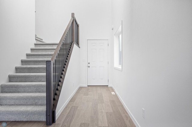 staircase with wood finished floors, baseboards, and a high ceiling