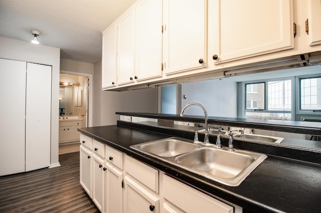 kitchen with a sink, a textured ceiling, white cabinetry, dark wood-style floors, and dark countertops