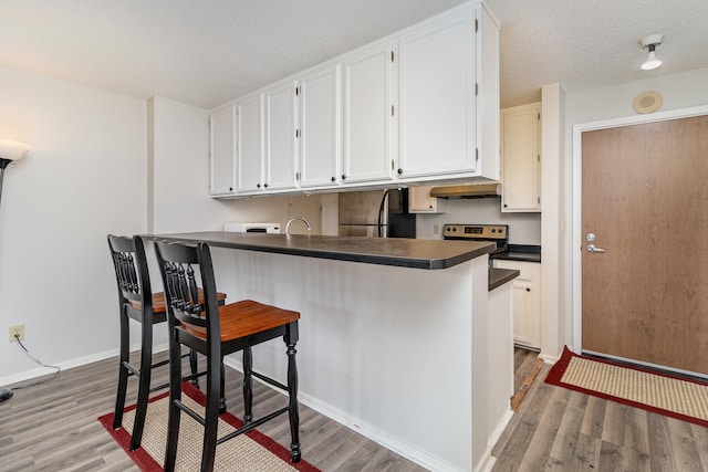kitchen featuring freestanding refrigerator, dark countertops, white cabinets, light wood-type flooring, and a textured ceiling