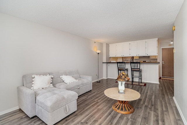living area featuring a textured ceiling, dark wood-style flooring, and baseboards
