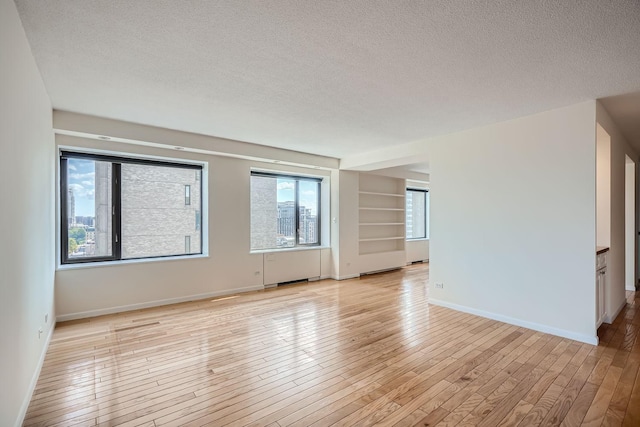 unfurnished room featuring light hardwood / wood-style flooring, a textured ceiling, and built in features