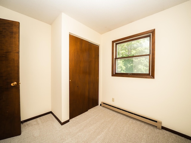 unfurnished bedroom featuring light colored carpet, a closet, and baseboard heating