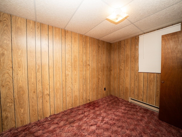 carpeted spare room featuring wood walls and baseboard heating