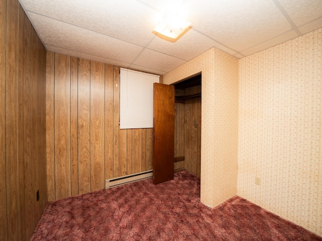 unfurnished bedroom featuring dark carpet, a closet, baseboard heating, and a paneled ceiling