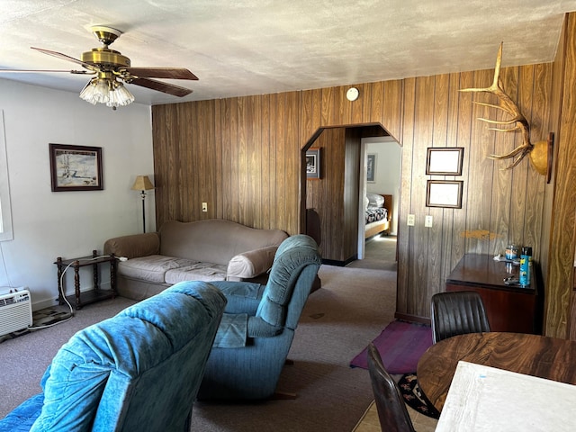 living room featuring a textured ceiling, carpet, wooden walls, and ceiling fan