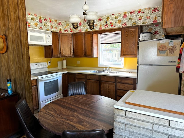 kitchen with white appliances, brown cabinetry, light countertops, a sink, and a notable chandelier