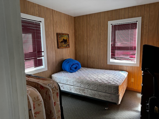 carpeted bedroom featuring wooden walls and multiple windows