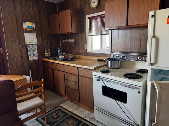 kitchen featuring wooden walls, white appliances, light countertops, and a sink
