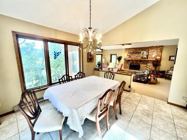 tiled dining room with a brick fireplace, a notable chandelier, and lofted ceiling