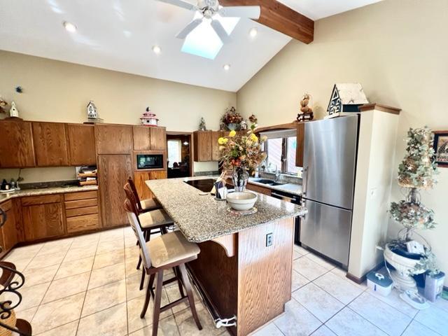 kitchen with beamed ceiling, a center island, stainless steel refrigerator, a kitchen breakfast bar, and a skylight