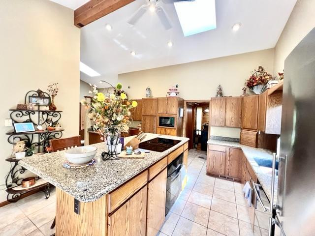 kitchen with black appliances, a kitchen island, vaulted ceiling with skylight, and light tile patterned floors