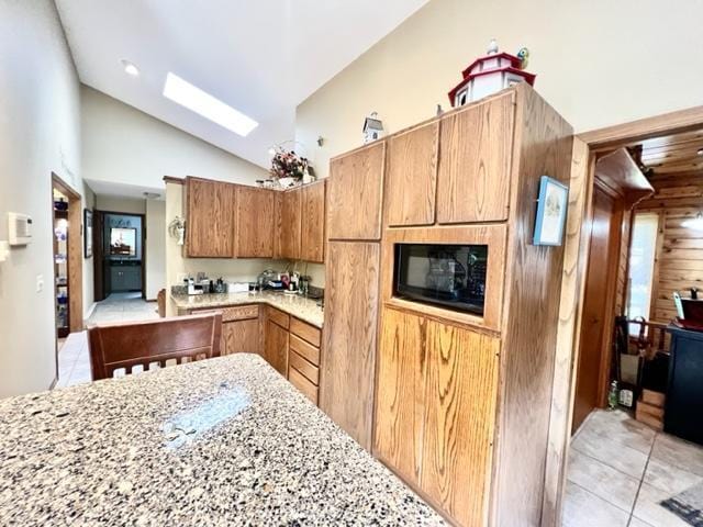 kitchen with light stone counters, a skylight, wood walls, light tile patterned floors, and high vaulted ceiling