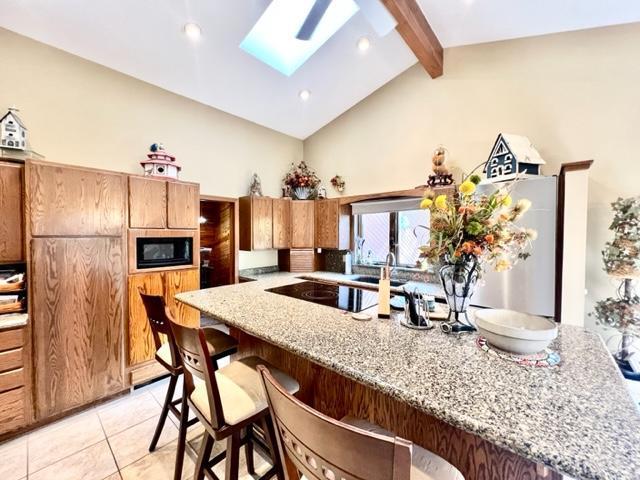 kitchen featuring light stone counters, a breakfast bar, light tile patterned floors, black appliances, and vaulted ceiling with skylight