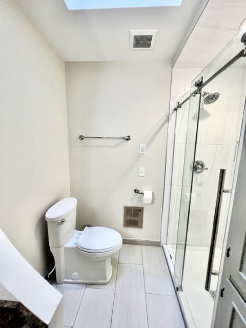 bathroom featuring walk in shower, toilet, and a skylight