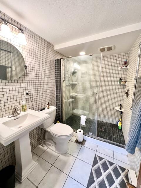 bathroom with tile walls, toilet, and an enclosed shower