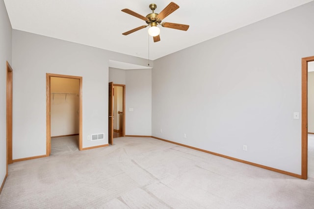 unfurnished bedroom with ceiling fan, a spacious closet, light carpet, and a closet