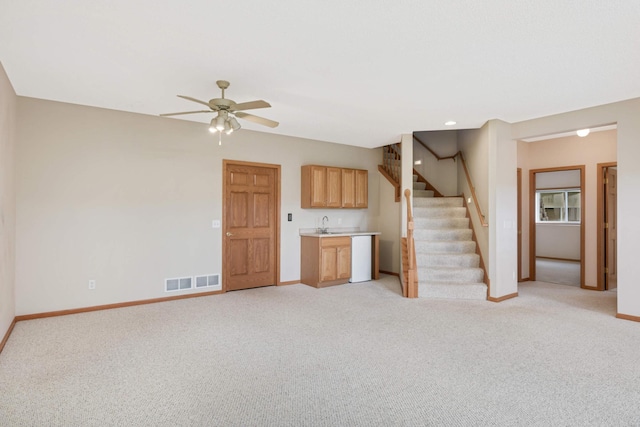 unfurnished living room featuring ceiling fan, light carpet, and bar area