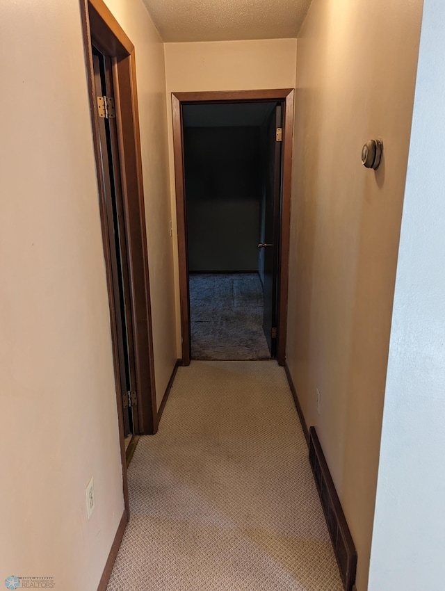 hall with a textured ceiling and light colored carpet