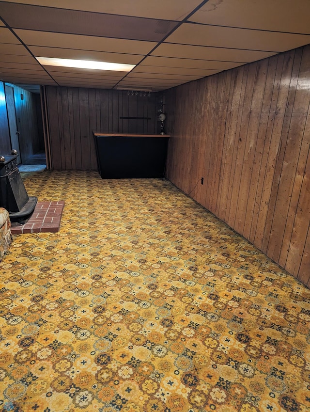 basement featuring a wood stove, wooden walls, and a drop ceiling