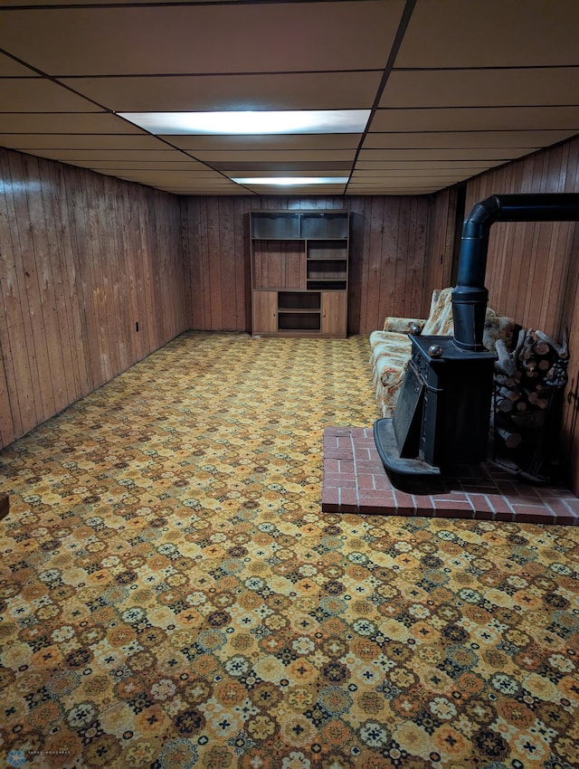 basement with wooden walls, a drop ceiling, and a wood stove