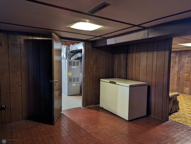 basement featuring refrigerator, wood walls, and heating unit