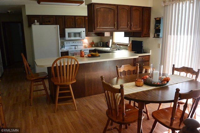 kitchen with dark brown cabinetry, sink, kitchen peninsula, white appliances, and dark hardwood / wood-style flooring