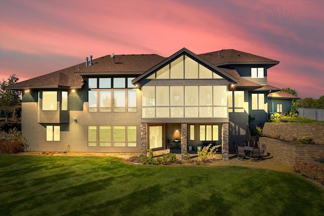 back house at dusk with a lawn and a patio area