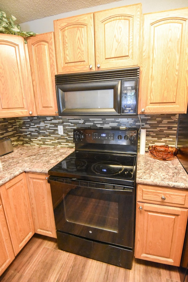 kitchen with black appliances, a textured ceiling, light stone counters, and light hardwood / wood-style floors