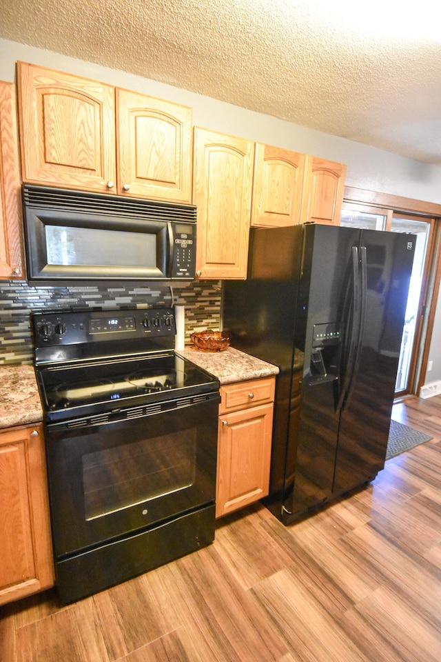 kitchen featuring a textured ceiling, black appliances, light hardwood / wood-style floors, and decorative backsplash