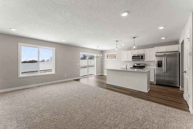 kitchen with pendant lighting, white cabinets, dark colored carpet, an island with sink, and stainless steel appliances