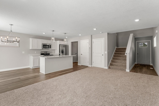 kitchen with appliances with stainless steel finishes, dark carpet, pendant lighting, white cabinetry, and an island with sink