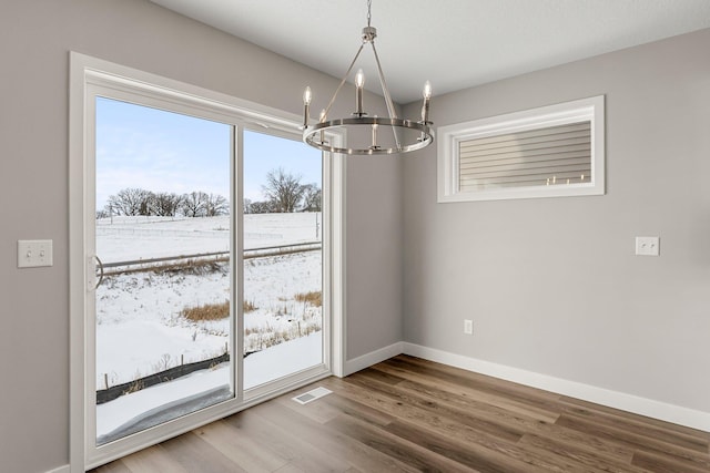 unfurnished dining area with a chandelier, wood-type flooring, and a healthy amount of sunlight