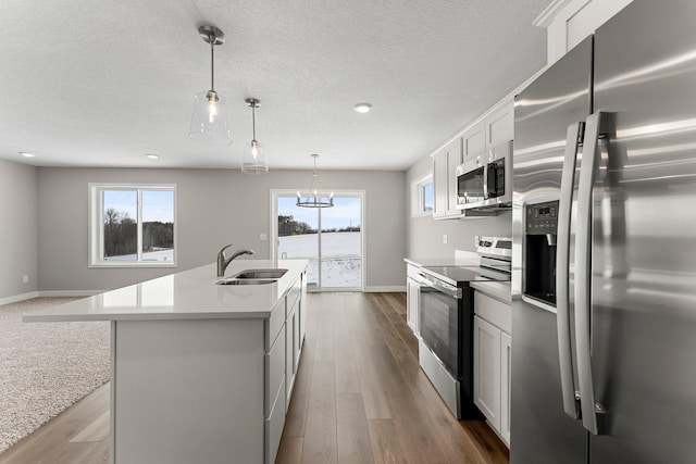 kitchen featuring a kitchen island with sink, sink, appliances with stainless steel finishes, decorative light fixtures, and white cabinetry