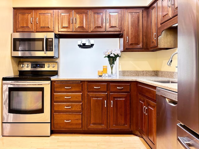 kitchen with light stone countertops, sink, light hardwood / wood-style flooring, and appliances with stainless steel finishes