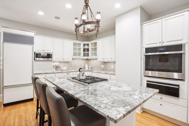 kitchen featuring an island with sink, tasteful backsplash, decorative light fixtures, light hardwood / wood-style flooring, and built in appliances