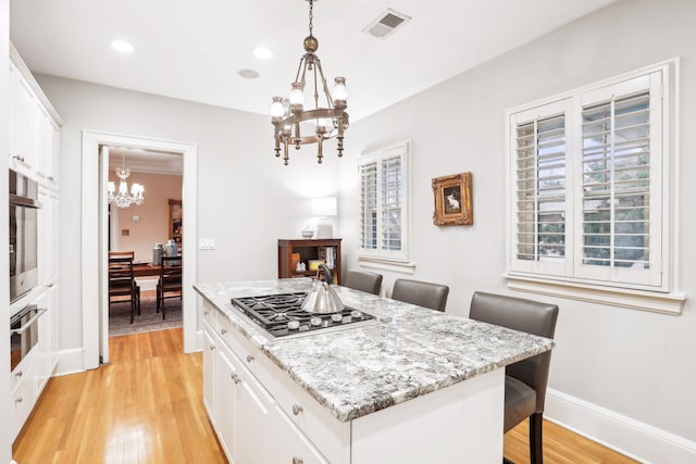 kitchen featuring light hardwood / wood-style flooring, appliances with stainless steel finishes, decorative light fixtures, and a kitchen island