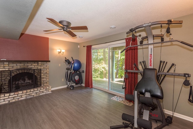 workout area with a brick fireplace, a textured ceiling, dark hardwood / wood-style floors, and ceiling fan