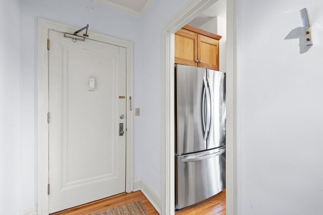 kitchen with light brown cabinets, light hardwood / wood-style flooring, stainless steel fridge, and ornamental molding